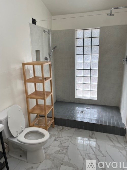 A bathroom with a toilet, a wooden shelf, and a shower.