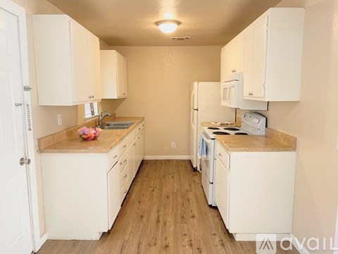 A kitchen with white cabinets and appliances, a wooden floor, and a white door.