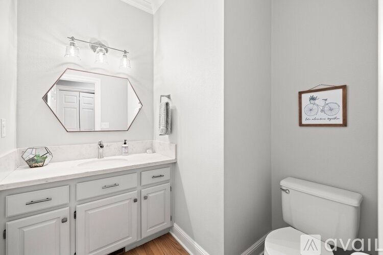 A white bathroom with a mirror, a toilet, and a framed picture on the wall.