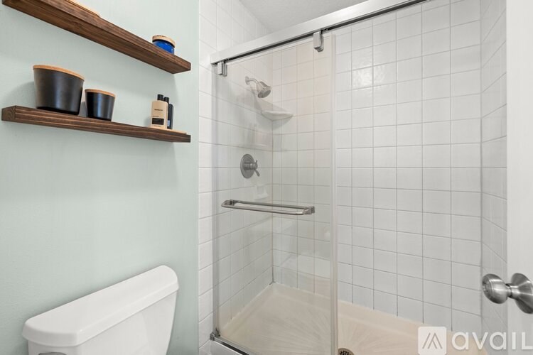 A bathroom with a toilet, a shower with a glass door, and shelves above the toilet.