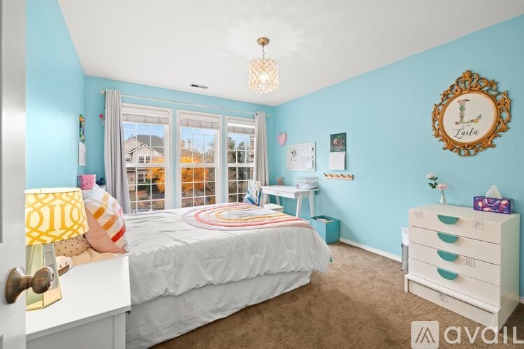 A bedroom with a white bed, a white dresser, and a window with a view of a residential area.