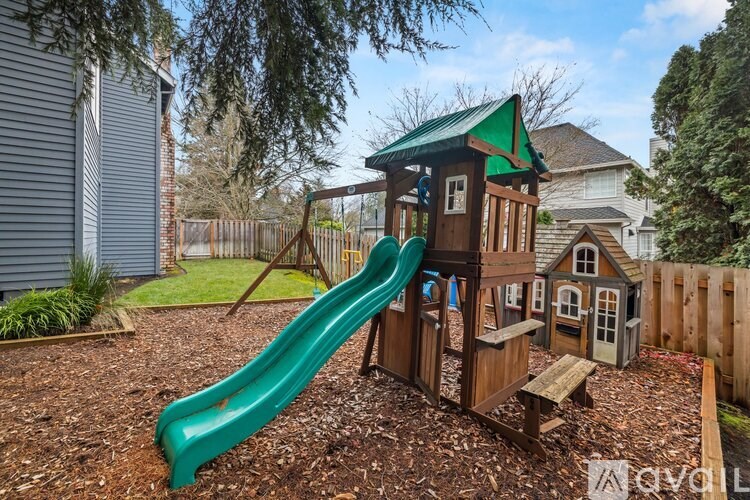 A wooden playset with a green slide in a backyard.