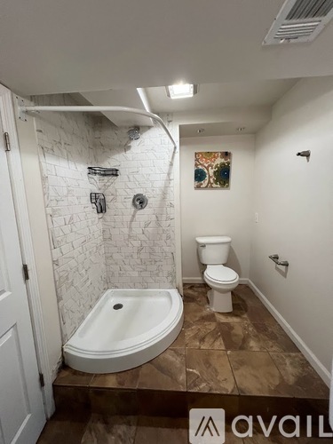 A bathroom with a white tiled shower and brown tiled floor.