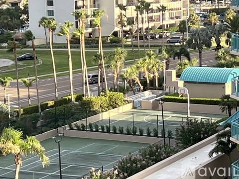 Tennis court surrounded by palm trees and buildings.