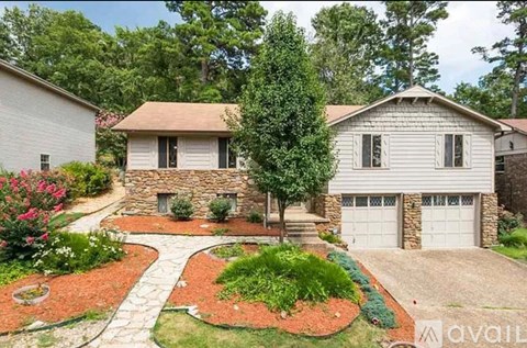 A house with a stone wall and a garage is surrounded by a garden with a red brick path.