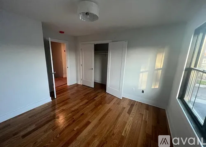 A room with wooden floors and white walls, with a window on the right side.