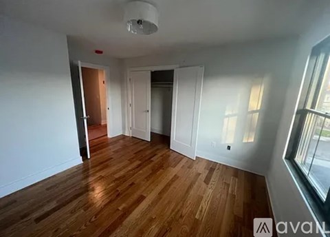 A room with wooden floors and white walls, with a window on the right side.