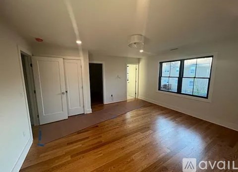 A spacious room with wooden flooring and a large window.