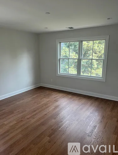 A room with wooden flooring and a window showing trees outside.