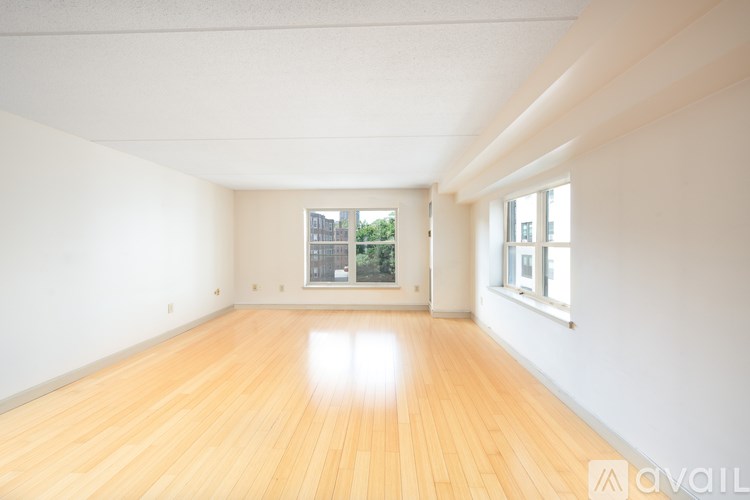 A room with wooden floors and white walls, with a window showing a view of trees and buildings outside.