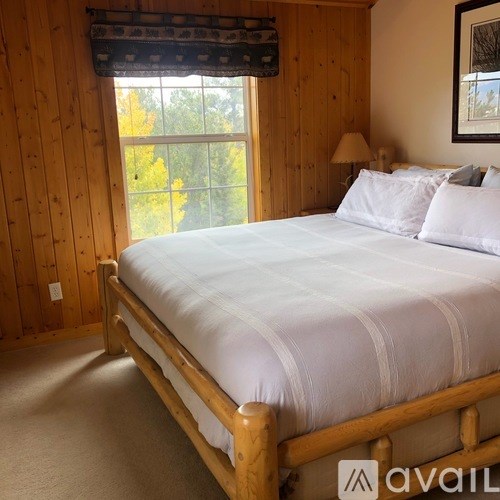 A bed with white sheets and a wooden frame in a room with wooden walls.