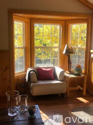 A cozy living room with a couch, a table with glasses and cups, and a view of trees through the window.