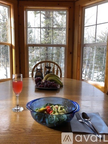 A bowl of salad sits on a table in front of a window with a view of trees.