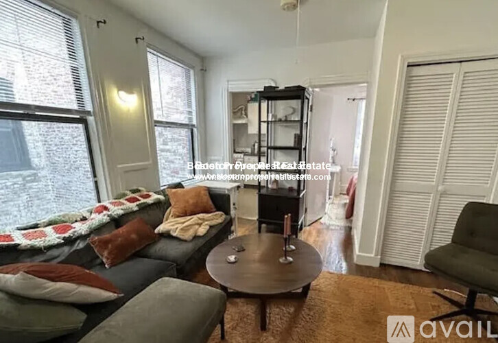 A living room with a grey couch, a coffee table, and a window with blinds.