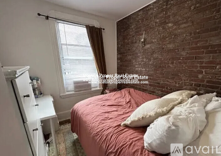A bedroom with a brick wall and a bed with a red comforter.