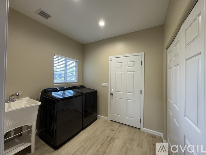 A kitchen area with a black fridge, white sink, and wooden flooring.