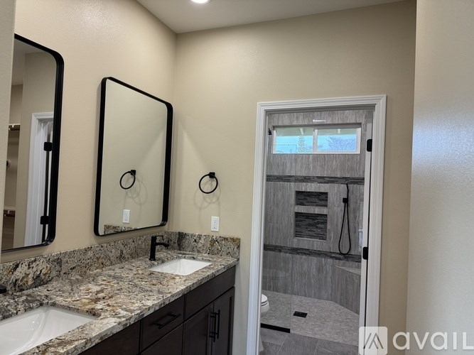 A bathroom with a granite countertop and a doorway to a shower.