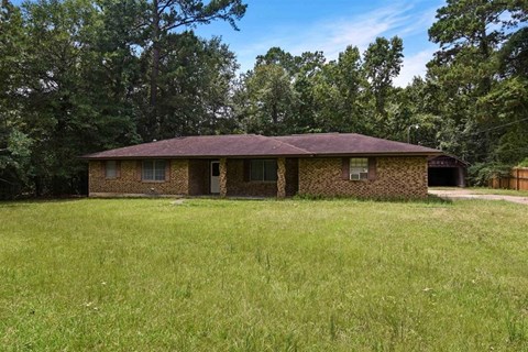 A house with a brown roof is surrounded by a grassy field.