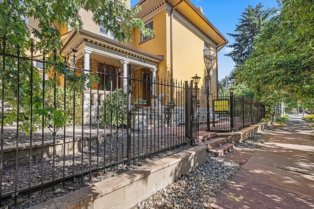 A yellow house with a black fence and a stone pathway leading to the front door.