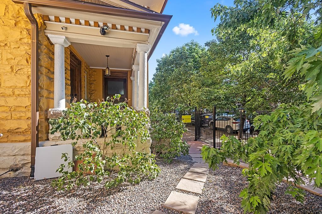 A yellow house with a porch and a gravel path leading to a gate.