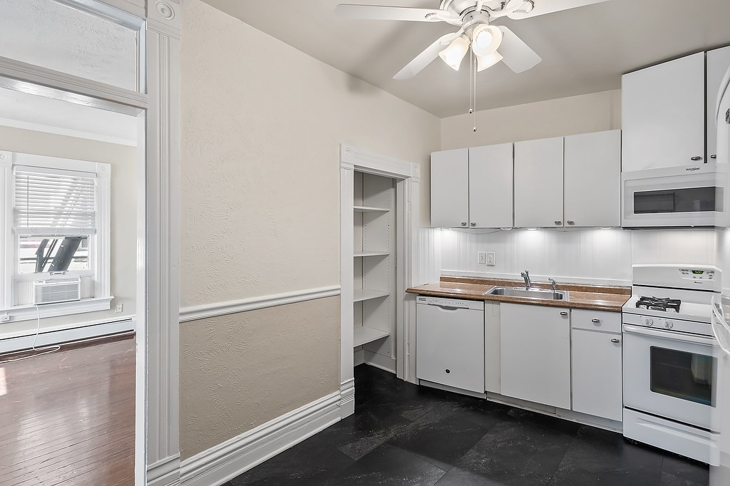 A kitchen with white cabinets and a black floor.