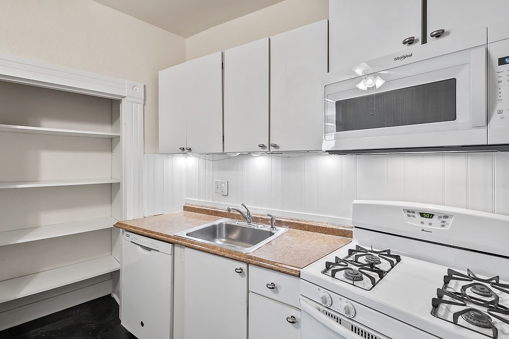 A white kitchen with a stove, sink, and cabinets.