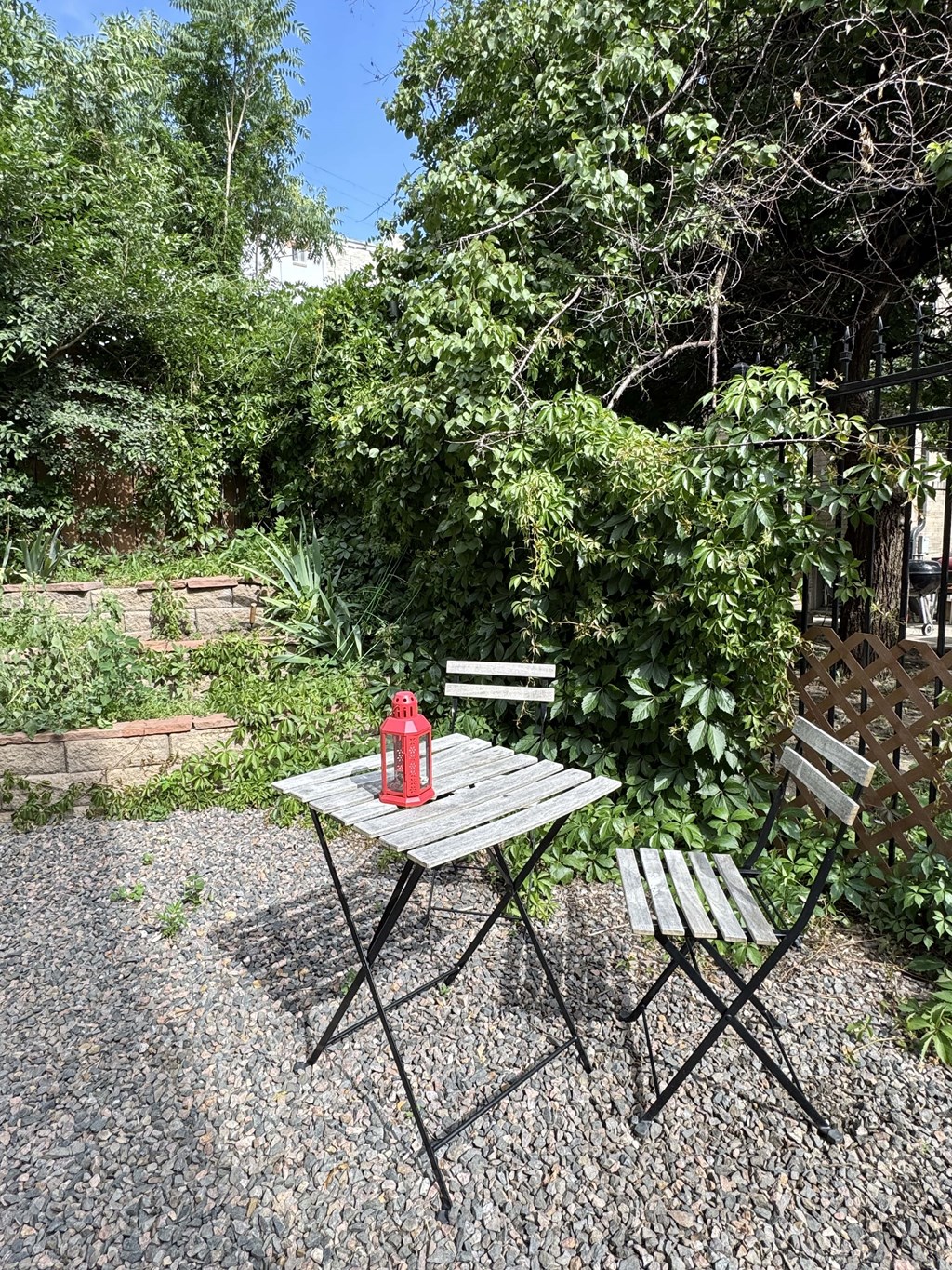 A table with a red lantern on it and a bench in front of a bush.