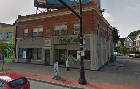 A street view of a building with a red car parked in front.