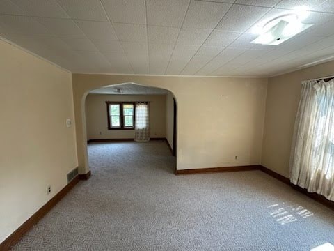 A spacious room with a carpeted floor and a window with curtains.