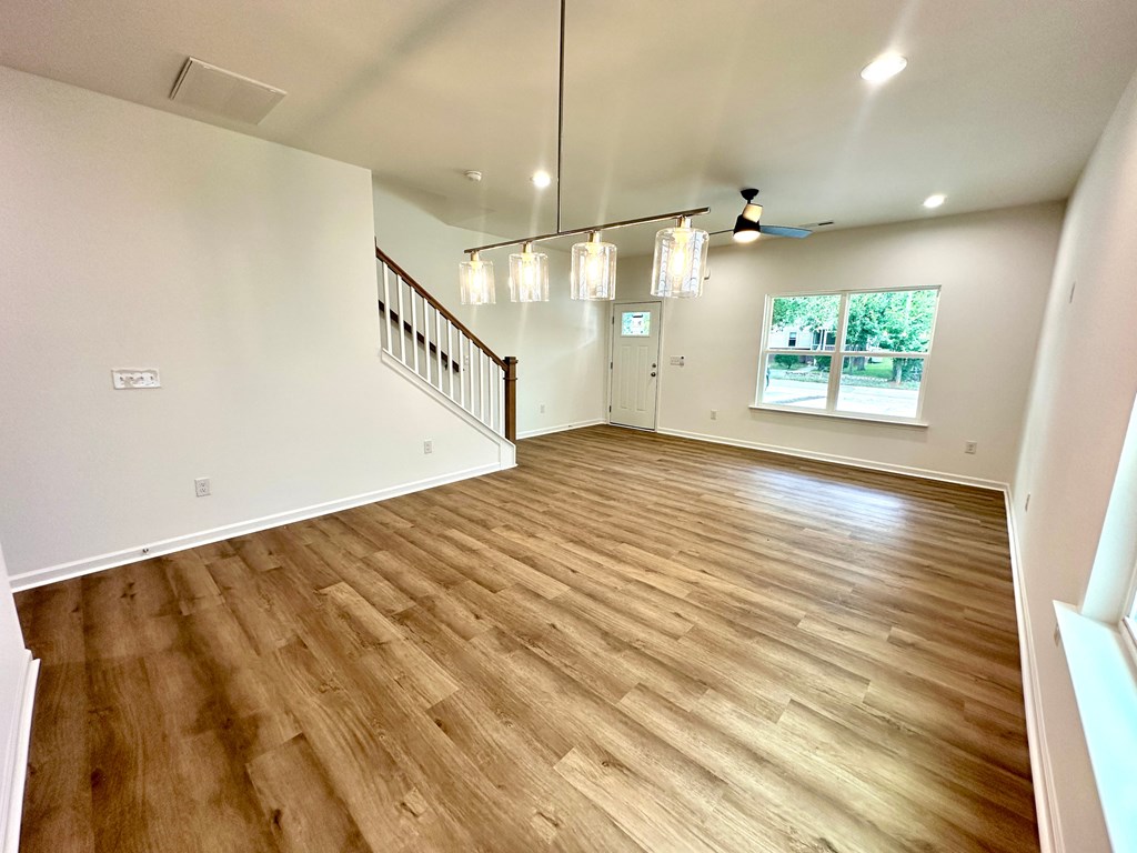 A spacious room with wooden flooring and a staircase.