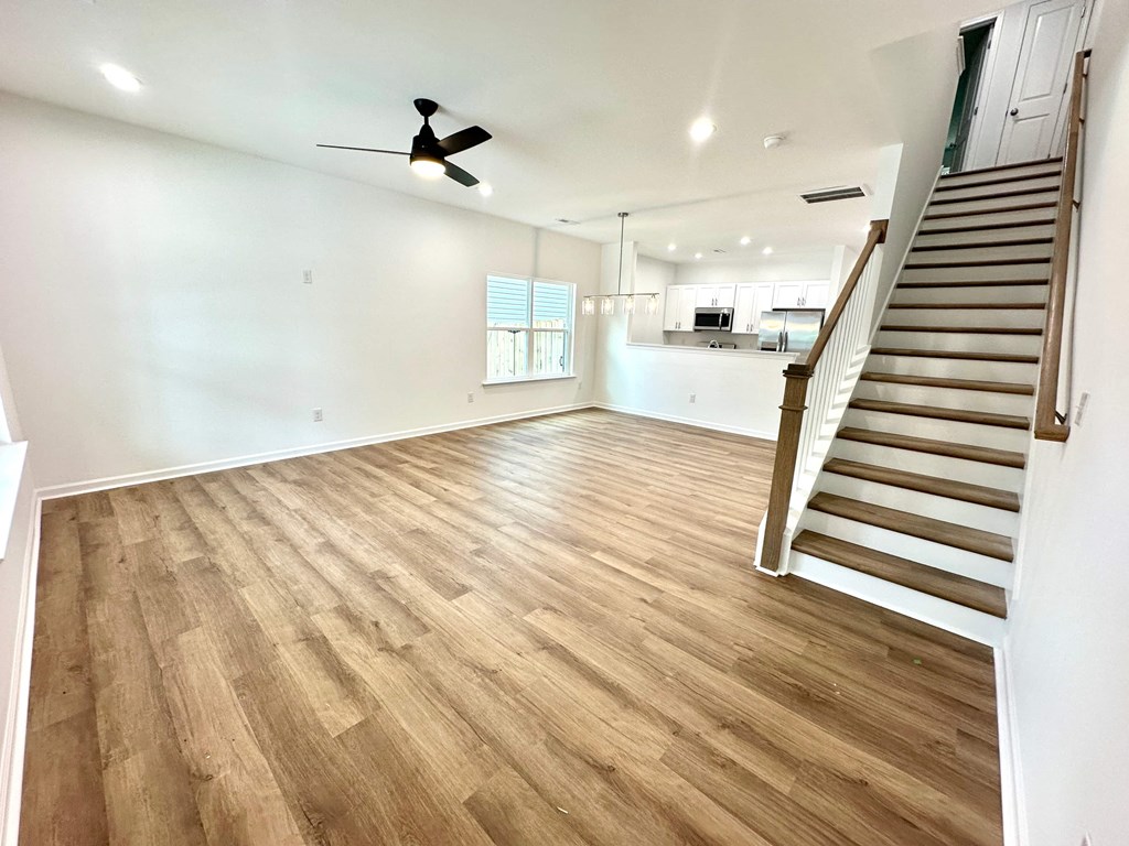 A spacious room with wooden flooring and a staircase.