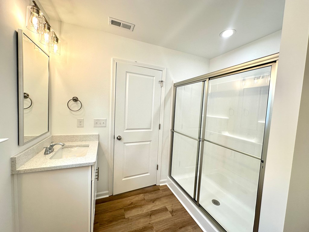 A white bathroom with a sink, mirror, and shower.