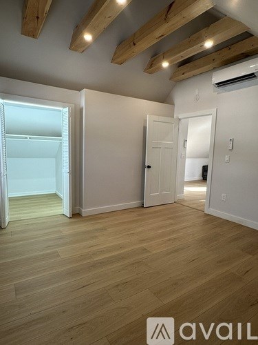 A room with wooden floors and white walls, with a door on the left and a window on the right.