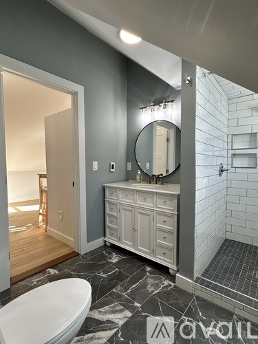 A bathroom with a white toilet and a white cabinet with a round mirror above it.
