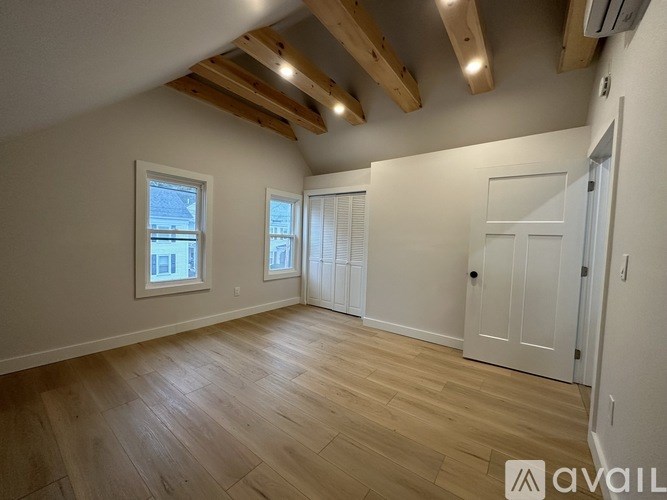 A spacious room with wooden flooring and white walls, featuring a door and two windows.