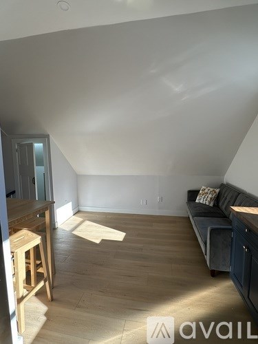 A living room with a couch, a bar stool, and a kitchenette.