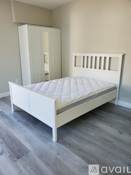 A white bed with a mattress and a wooden floor.