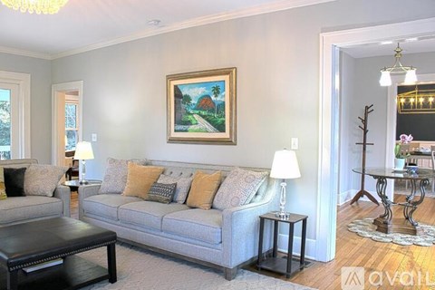 A living room with a grey couch, a painting on the wall, and a chandelier hanging from the ceiling.