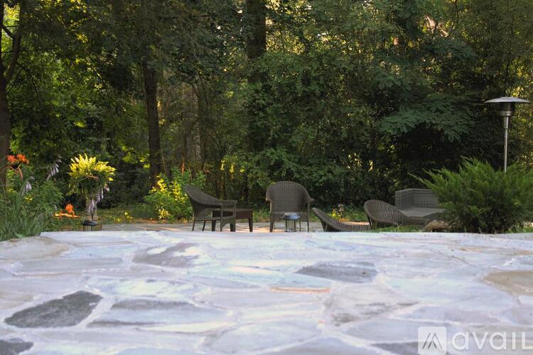 A patio with chairs and a stone floor surrounded by trees.