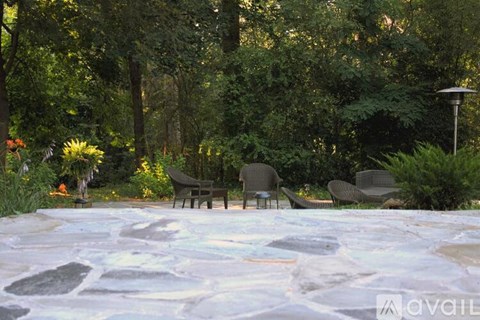 A patio with chairs and a stone floor surrounded by trees.