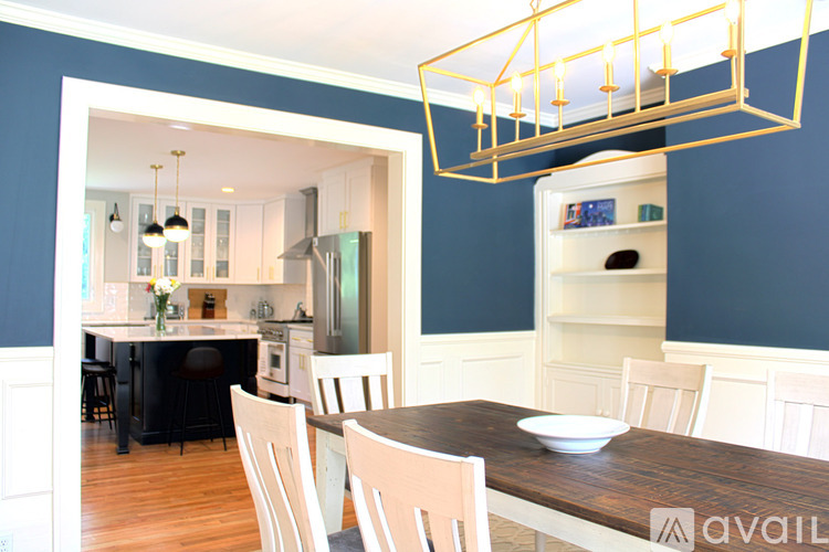 A dining room with a table and chairs and a kitchen in the background.
