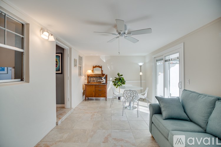 A living room with a grey couch, a wooden cabinet, a white chair, and a ceiling fan.
