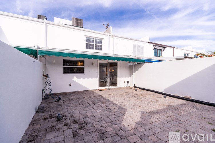 A white building with a green awning and a brick patio.