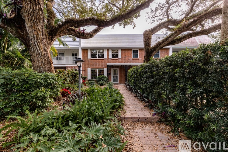 A house with a red brick facade is surrounded by greenery and a pathway leading to the entrance.
