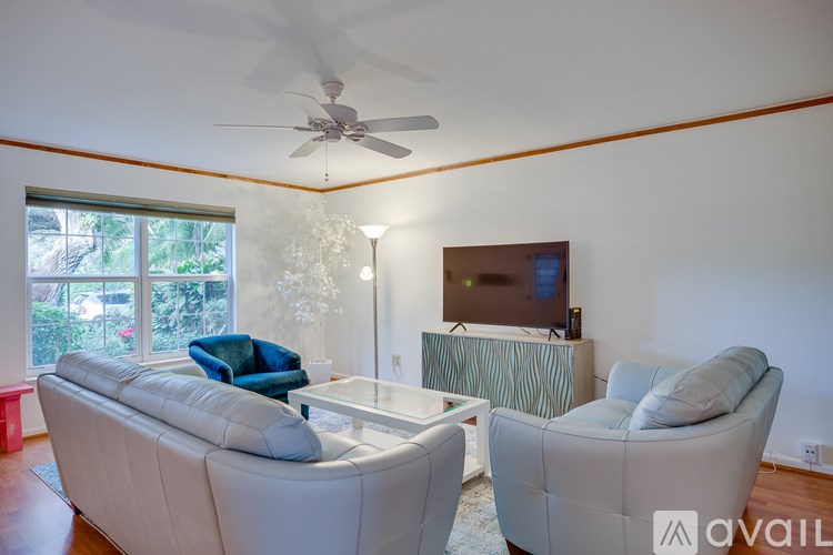 A living room with a white couch, a blue chair, a television, and a ceiling fan.