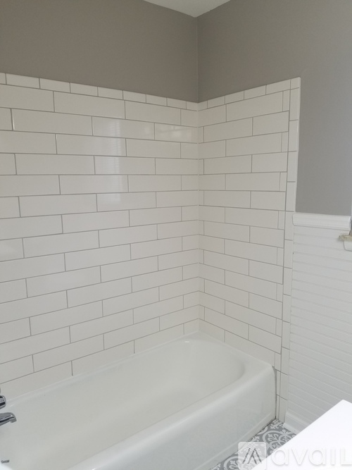 A white bathtub in a bathroom with white tiled walls.