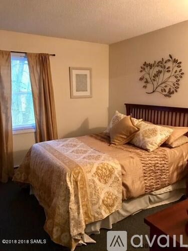 A bedroom with a bed covered in a patterned bedspread and a wall art of a tree.
