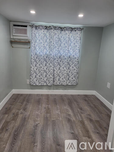 A room with a wooden floor and a window with a curtain.