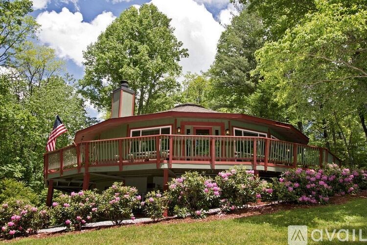 A house with a red roof and a balcony surrounded by green trees and bushes.