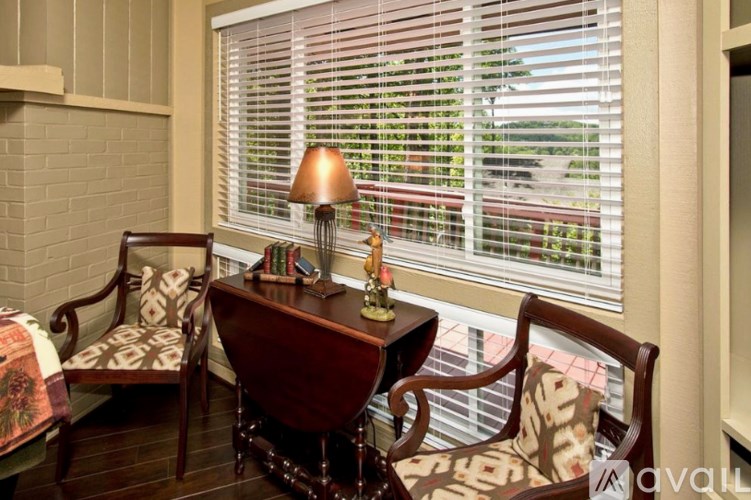 A table with a lamp and a chair in front of a window with blinds.